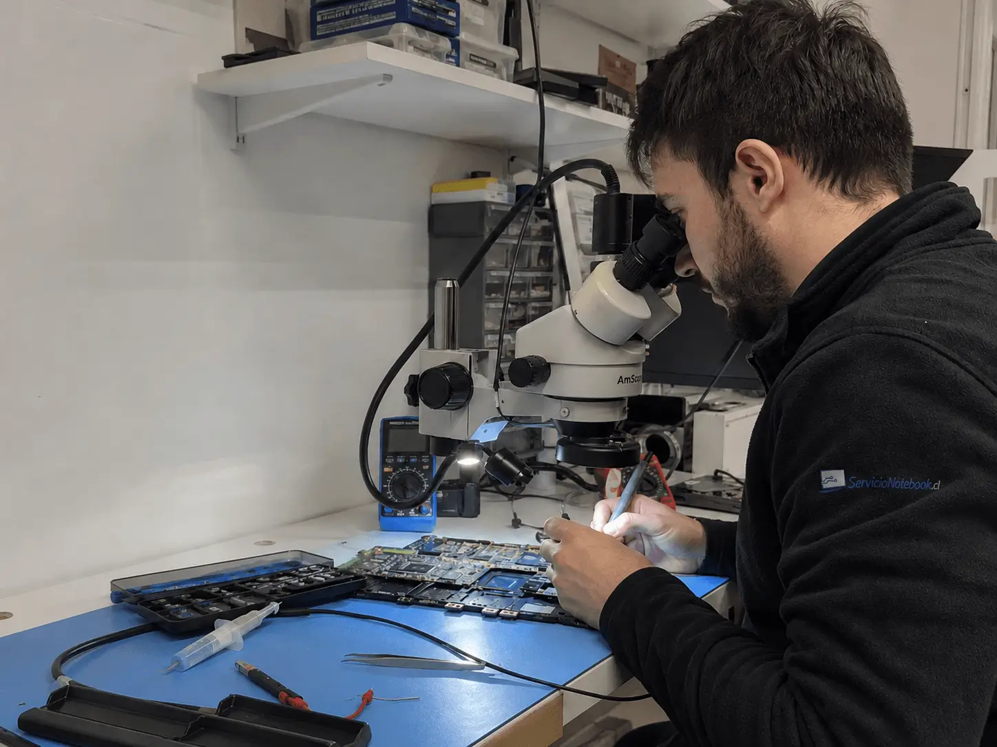 Técnico reparando una placa madre de notebook con microscopio